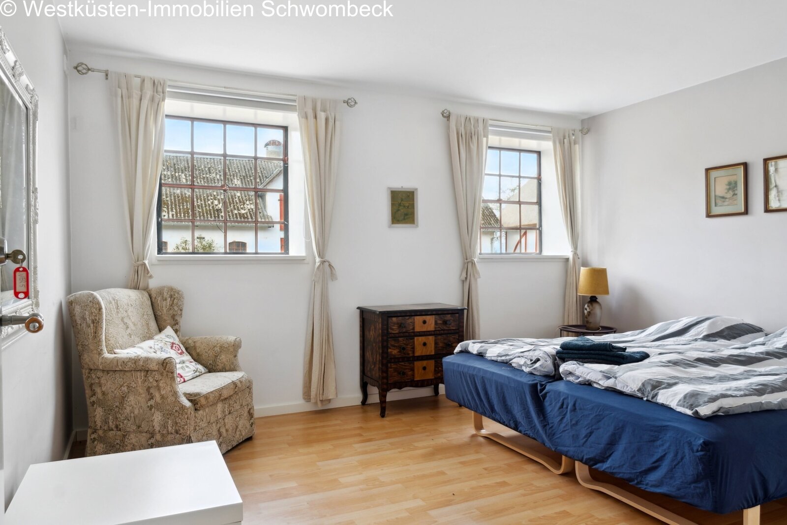 Helles Schlafzimmer mit zwei großflächigen Fenstern und Holzparkettboden