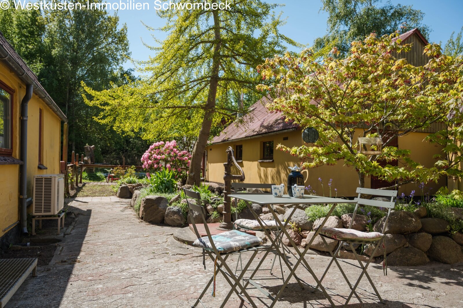 Terrasse mit schattenspendendem Baumbestand und naturnahem Freisitzbereich