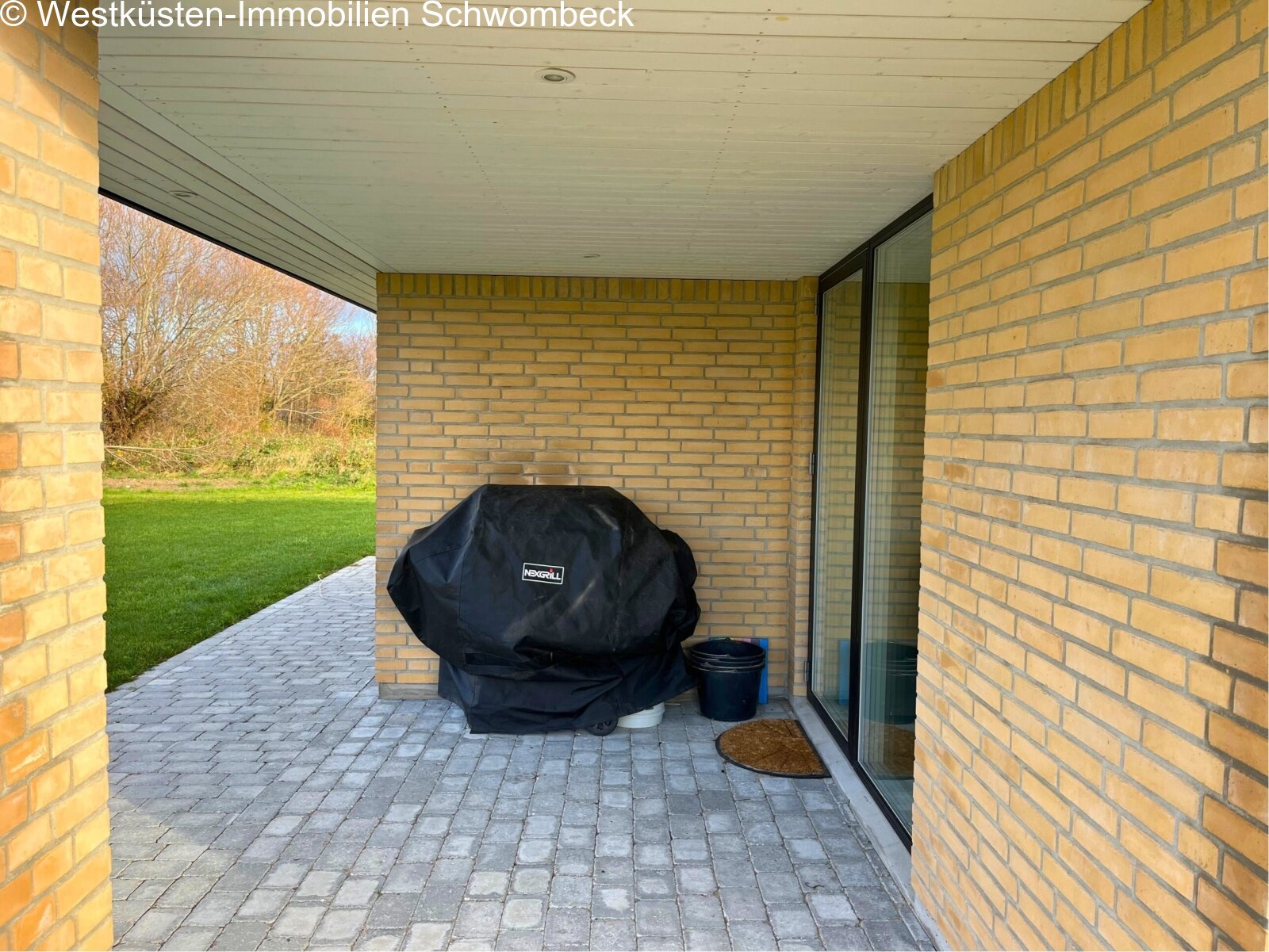 Überdachte Terrasse mit hochwertiger Natursteinpflasterung und direktem Gartenübergang